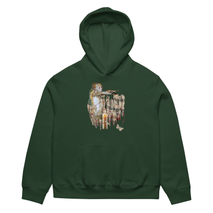 A dark forest green pullover hoodie with a detailed graphic print on the chest depicting a vintage-style painting of a child, candles, and butterflies.