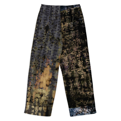 A pair of wide-leg cropped pants featuring a split design: one leg has a distressed gray and black pattern with gold accents, while the other leg has a black background covered in white graffiti-style text and paint splatters.